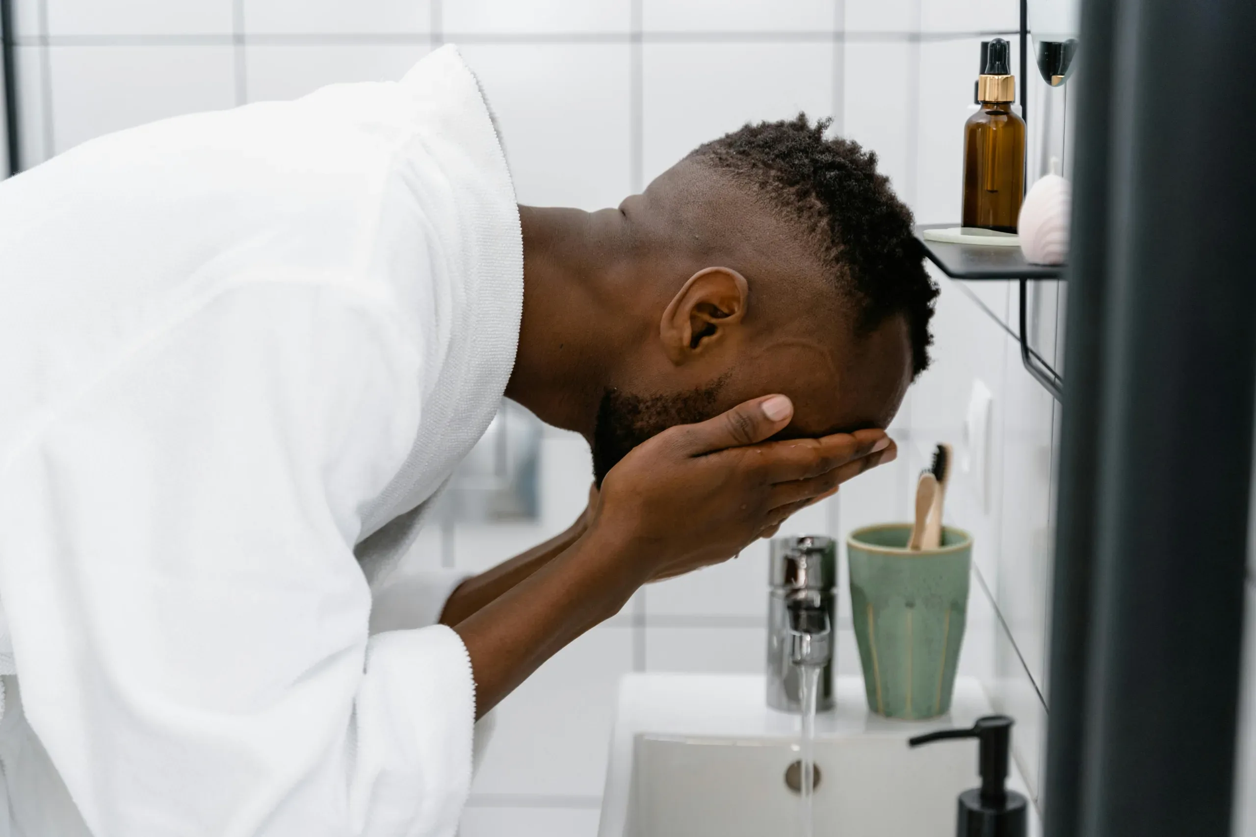 a man wearing a white robe washes his face over a sink